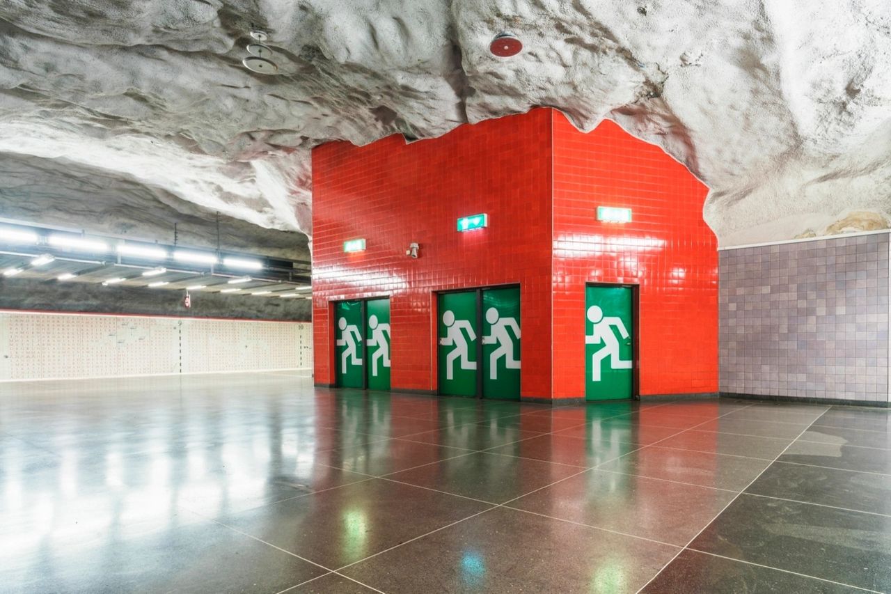 Underground station concourse in Stockholm, Sweden, with rock ceiling and red tiled structure. Illustrative image, not an identified shelter.